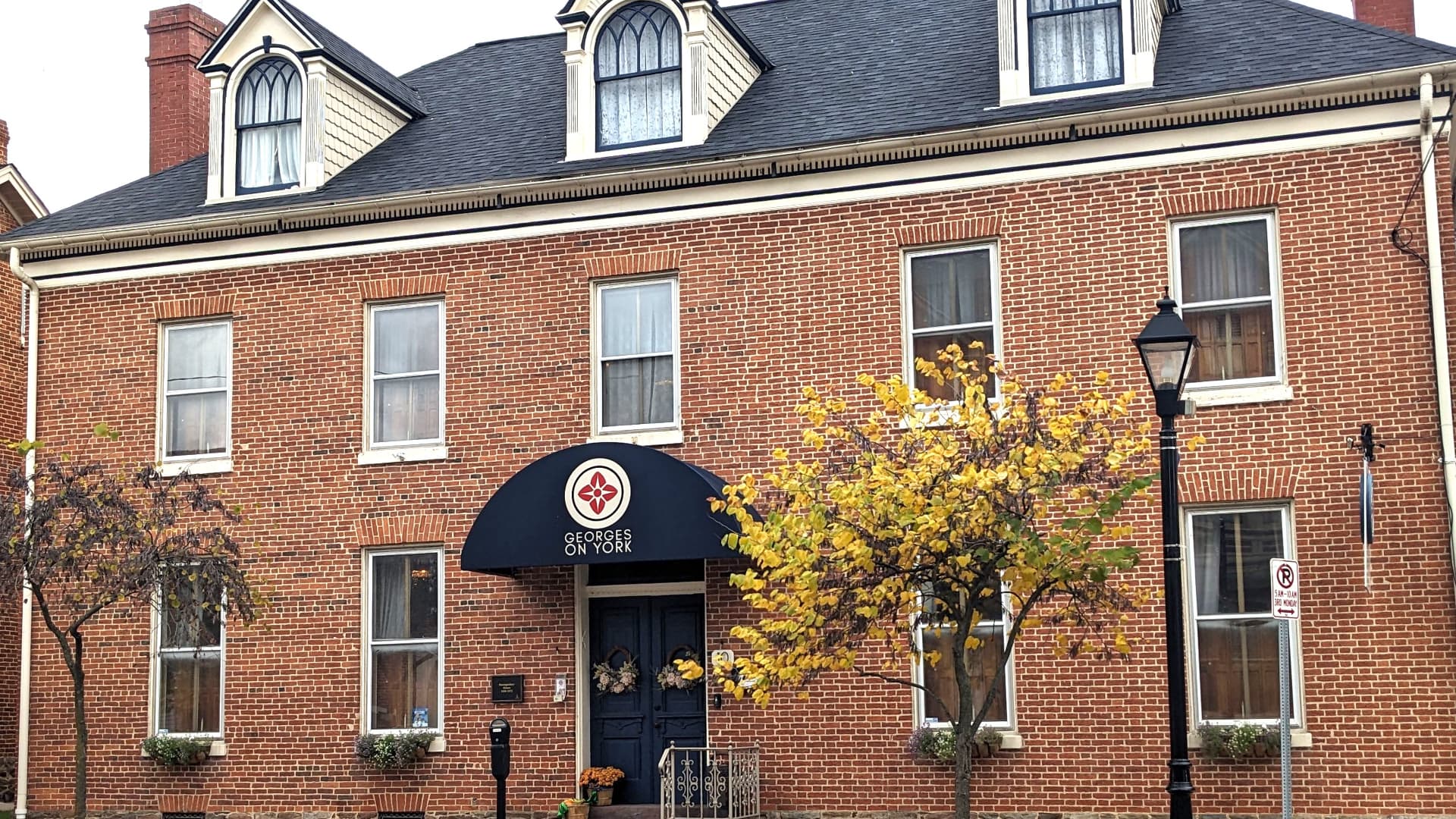 Brick building with an arched entrance and yellow trees in front.
