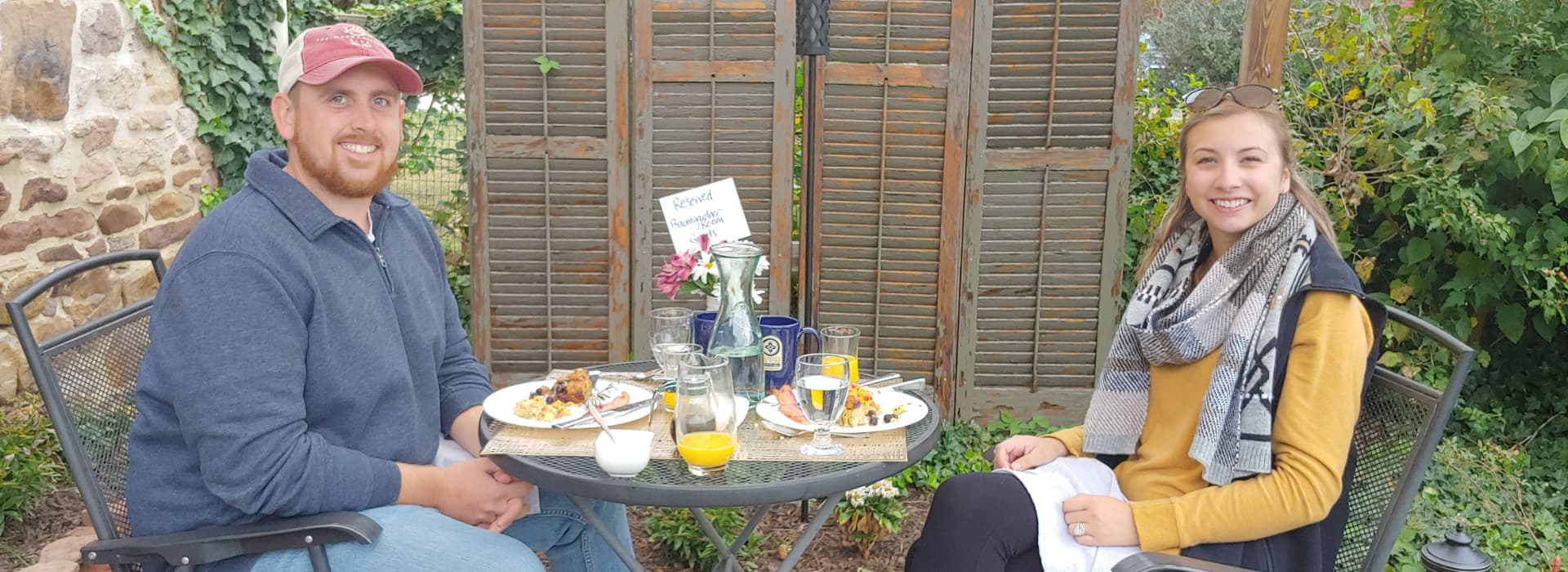 A man and a woman enjoy a meal together at a table in a garden setting.